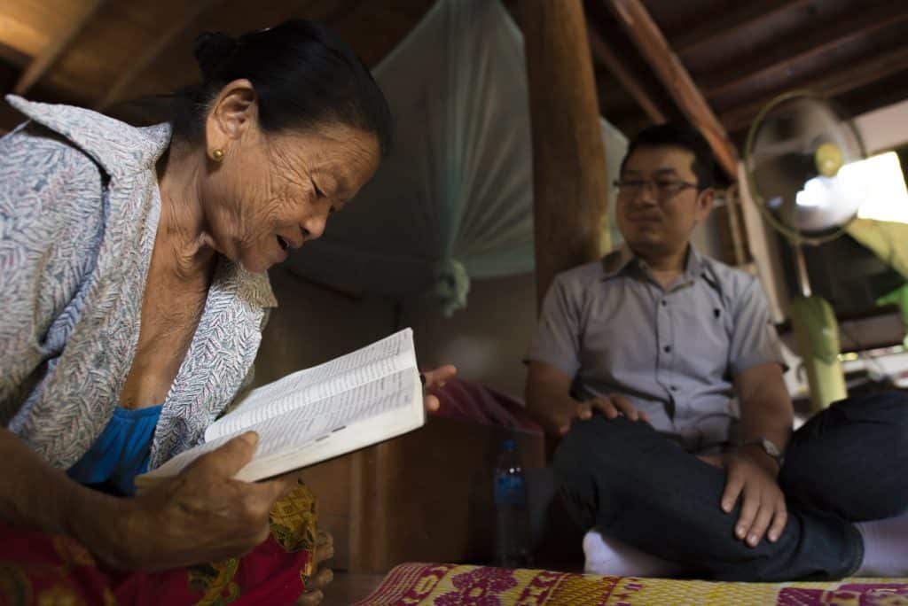 A woman reads the bible while a younger man looks on.